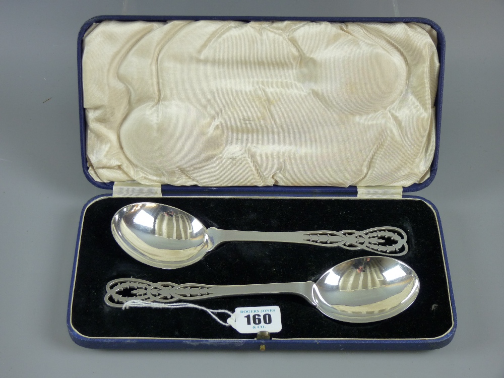 A cased pair of silver serving spoons having circular bowls and shaped handles with pierced bell