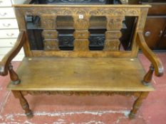 A circa 1900 carved oak hall bench with triple splatback and swept arms on baluster supports,