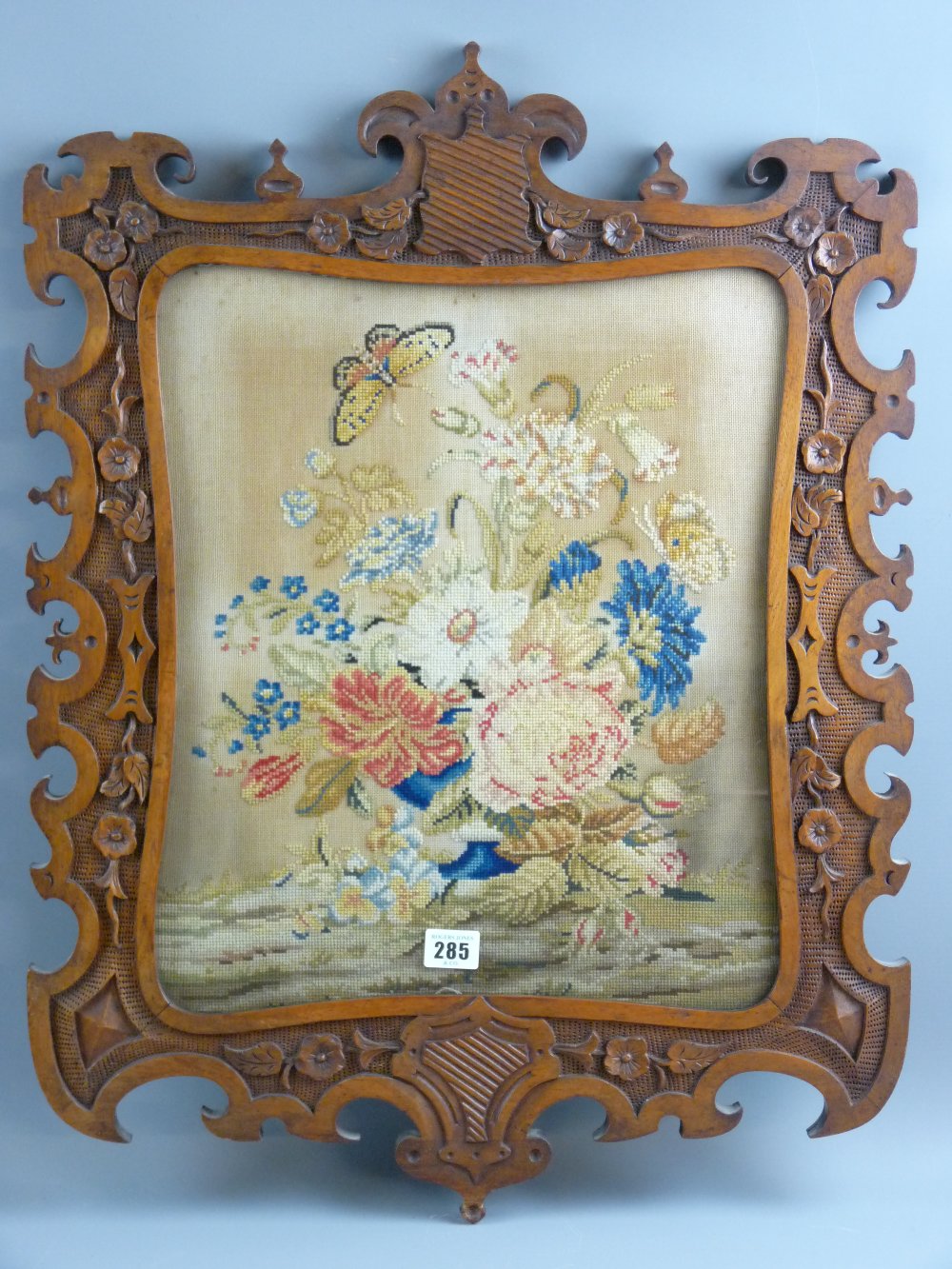 A late 19th Century woolwork floral panel with butterflies in a well carved floral decorated oak