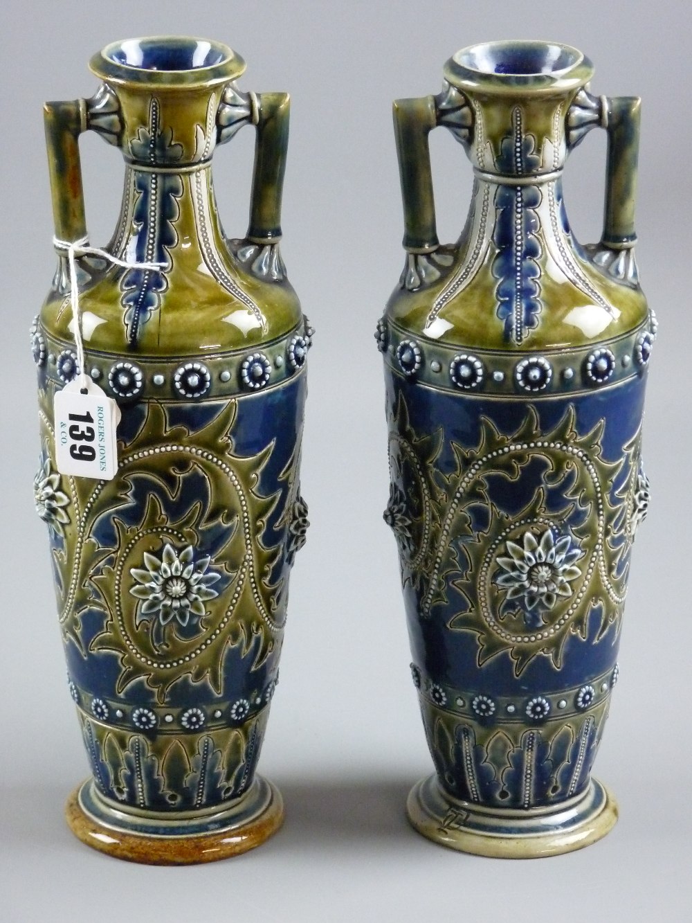 Doulton Lambeth stoneware - a near matching pair of twin handled vases of tapering form incised