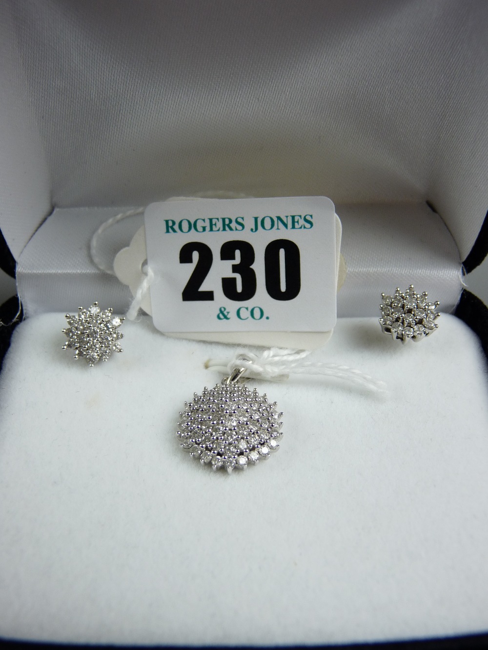 A white gold diamond pendant and earring set comprising a fine circular diamond cluster pendant of