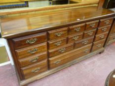 An antique style long mahogany chest of nine drawers with shaped brass backplates and swing