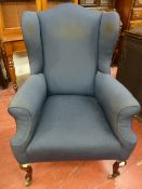 A circa 1900 wingback upholstered armchair with swept arms, shaped front supports and brass castors