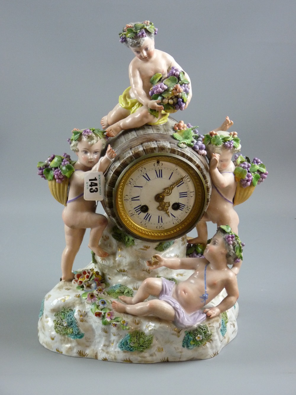 Meissen porcelain - a figural mantel clock with barrel clock housing on a floral encrusted and