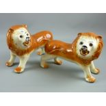 A pair of Staffordshire pottery standing lions with glass eyes, 25 x 35 cms