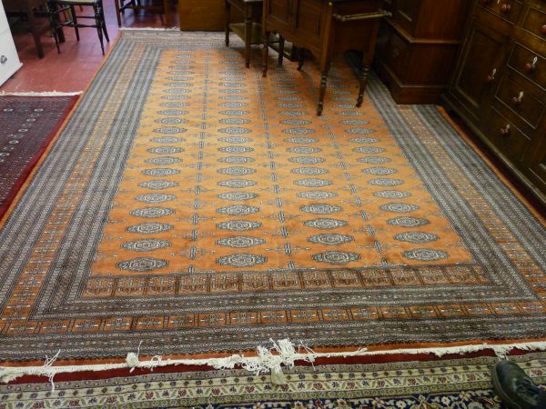 A LARGE PAKISTAN CARPET, rust ground multi bordered with tasselled ends and large block repeat