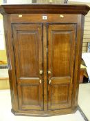 A GEORGIAN OAK HANGING CORNER CUPBOARD having two crossbanded twin panel slender doors with brass