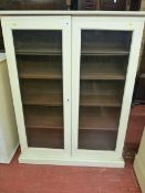 A PAINTED TWO DOOR BOOKCASE having twin glazed doors with interior adjustable shelves on a stepped