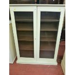 A PAINTED TWO DOOR BOOKCASE having twin glazed doors with interior adjustable shelves on a stepped