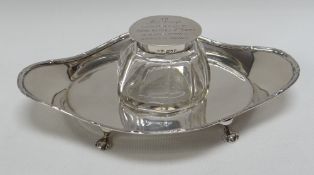 A SILVER INKSTAND of dish form on four pad feet and single faceted inkwell with inscribed lid,