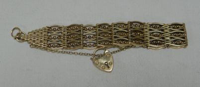 A 9CT YELLOW GOLD BRACELET of wavy and twist gate form and with heart-shaped padlock, 46.9gms