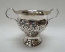 A SILVER TWIN-HANDLED VASE raised on a circular base and decorated with floral relief and sashes,