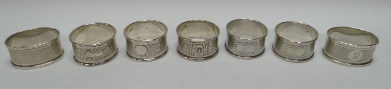 A SET OF FIVE CIRCULAR & A PAIR OF OVAL SILVER NAPKIN RINGS all machine turned with monograms,