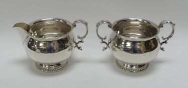 A MATCHING CIRCULAR BASED SILVER CREAM JUG & SUGAR BASIN with feathered rims and C-scroll handles,