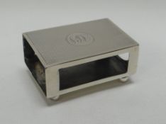 A SILVER TABLE-MATCHBOX HOLDER on ball feet and with machine turn decoration and monogram, London