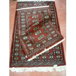 TWO EASTERN WOOLLEN RUGS, red ground, hand knotted Pakistan Bokhara with tasselled ends, 98 x 66 cms