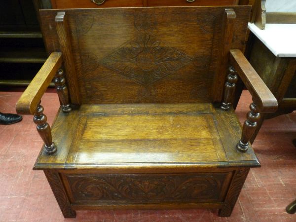 A CIRCA 1930's OAK MONK'S BENCH, the top floral carved to both sides with turned arm supports and