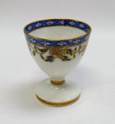A RARE SWANSEA PORCELAIN EGG CUP decorated with a continuous band of blue and gilded flowers and