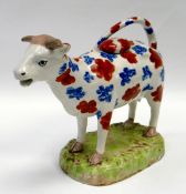 A SWANSEA POTTERY COW CREAMER standing on a grassy base, with looped tail as handle and decorated