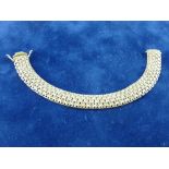 A NINE CARAT GOLD AND DIAMOND WIDE BANGLE of tapered form with pierced oval panels and five small
