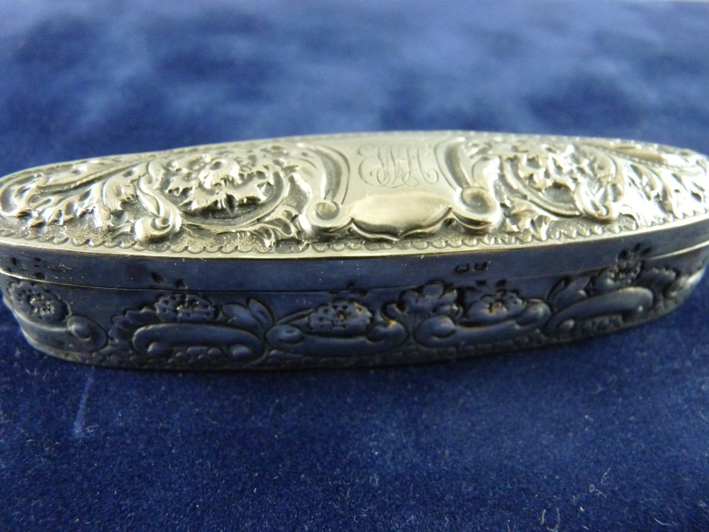 A HALLMARKED SILVER PILL BOX in elongated oval form with embossed floral decoration and central