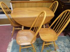 AN ERCOL LIGHT ELM DROP LEAF DINING TABLE AND FOUR CHAIRS having raised hoop with stick backs