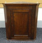 AN OAK HANGING CORNER CUPBOARD having a single door hinging to reveal a two shelved interior,