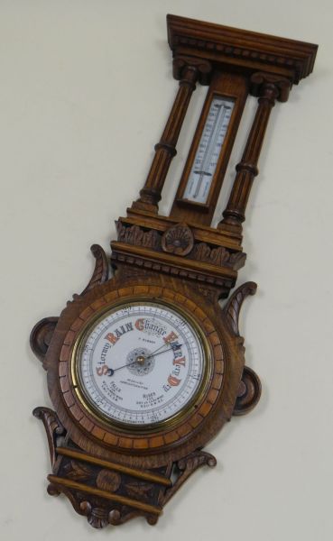 AN OAK ENCASED BAROMETER & THERMOMETER SET the case heavily carved with fluted pillars and having