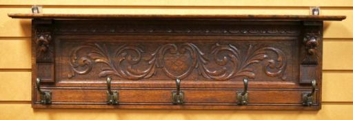 AN OAK COAT RAIL foliate carved and with lion-head supports and five metal hooks, 101cms wide