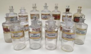 SEVENTEEN CLEAR GLASS PHARMACEUTICAL BOTTLES all with labels and of similar size, approx 20cms