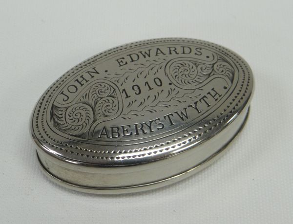 AN OVAL WHITE METAL TOBACCO BOX with hinged lid, the base and lid with sgraffito decoration and