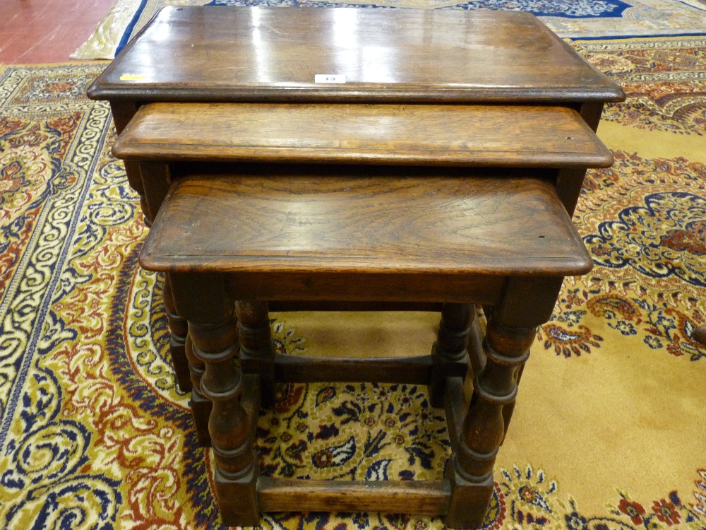 AN OAK NEST OF THREE TABLES in the rustic style with turned and block supports and oblong