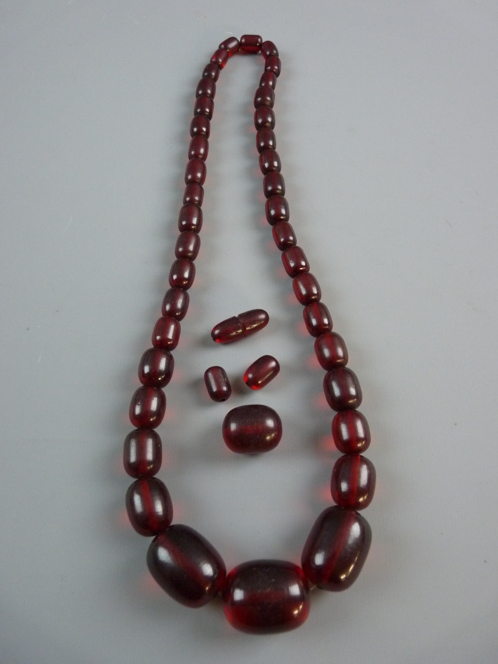 A DARK AMBER NECKLACE of graduated oblong beads and with four additional loose beads