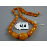 A GRADUATED SET OF EGG YOLK AMBER BEADS, approximate measurements 44 cms long, the largest bead 2