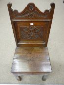 AN 18th CENTURY OAK HALL CHAIR having a shaped floral carved top rail, a floral carved back panel