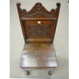 AN 18th CENTURY OAK HALL CHAIR having a shaped floral carved top rail, a floral carved back panel