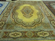 A MUSTARD GROUND KESHAN WOOL CARPET having a wide floral crimson and blue border and with a centre