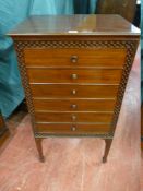 AN EDWARDIAN MAHOGANY MUSIC CABINET with blind fret front decoration and six drop front drawers with