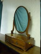 A SHERATON STYLE OVAL MAHOGANY TOILET MIRROR having shaped supports on a slightly curved two