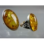TWO LARGE OVAL, BELIEVED SILVER, DRESS RINGS with amber stones, one 3 x 2 cms and the other 2.5 x