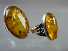 TWO LARGE OVAL, BELIEVED SILVER, DRESS RINGS with amber stones, one 3 x 2 cms and the other 2.5 x