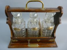 A VINTAGE OAK THREE BOTTLE TANTALUS with hallmarked silver labels having a brass carry handle and