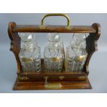 A VINTAGE OAK THREE BOTTLE TANTALUS with hallmarked silver labels having a brass carry handle and