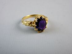 A NINE CARAT GOLD DRESS RING with decorative shoulders and oval purple stone, 3.2 grms total