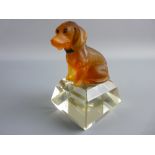 A FROSTED AMBER GLASS MODEL OF A SEATED DOG with inset eyes and a metal collar set upon a facet