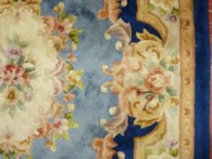 A 20th CENTURY WASHED WOOLLEN RECTANGULAR CARPET in tonal blues with floral design and tasseled