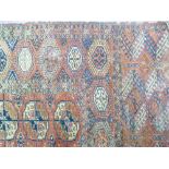 AN EASTERN RED GROUND WOOLLEN CARPET, wide bordered with central repeating block pattern, 305 x