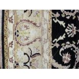 A GOOD BLACK GROUND AND CREAM BORDERED WOOLLEN CARPET, the central panel with opposing repeat