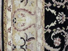 A GOOD BLACK GROUND AND CREAM BORDERED WOOLLEN CARPET, the central panel with opposing repeat