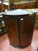 A GEORGIAN OAK BOW FRONT HANGING CORNER CUPBOARD with crossbanded doors and brass 'H' hinges and